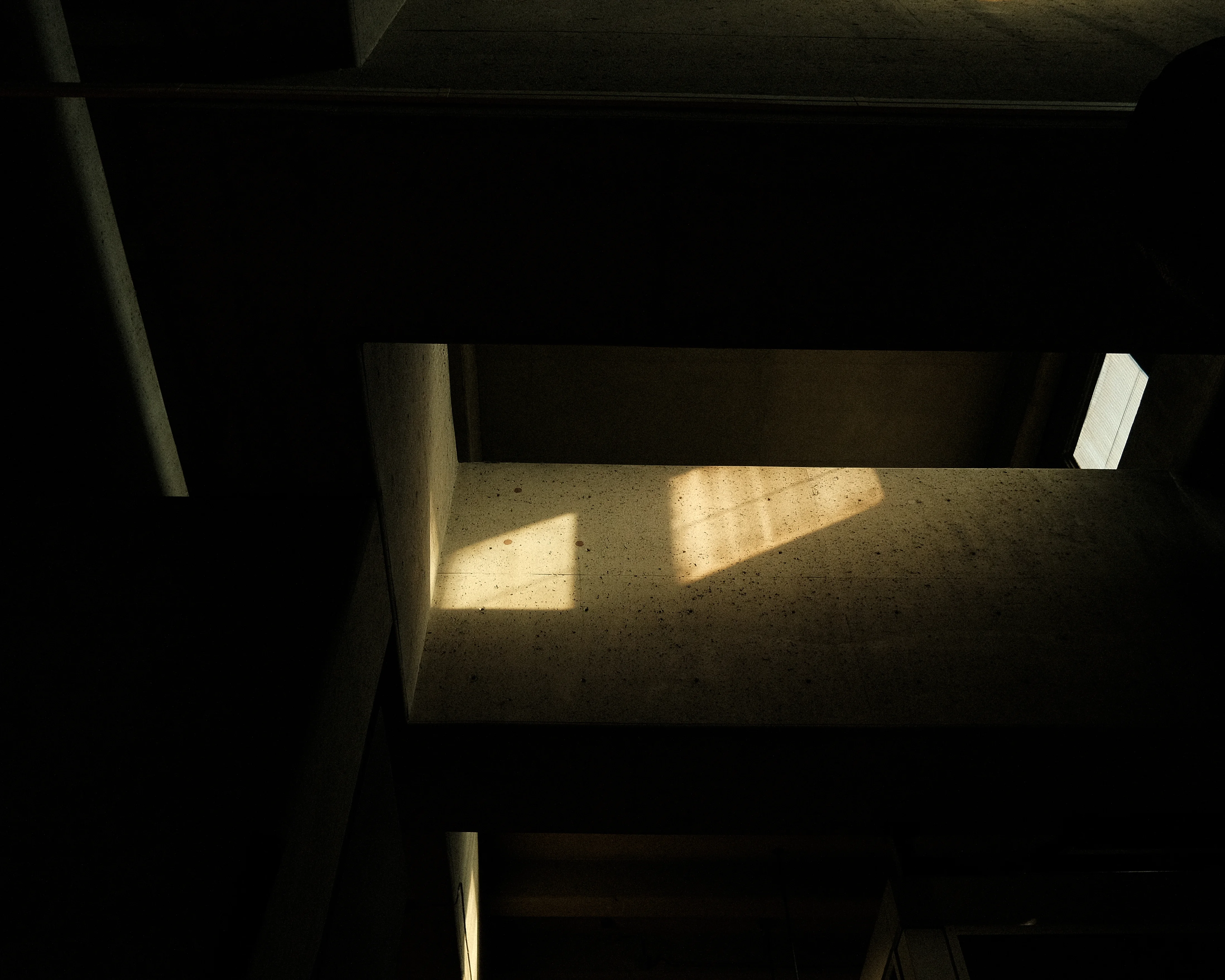 A narrow beam of light shines through a crack in a dark, concrete ceiling. The light illuminates a small section of the ceiling and casts a shadow on the wall below.