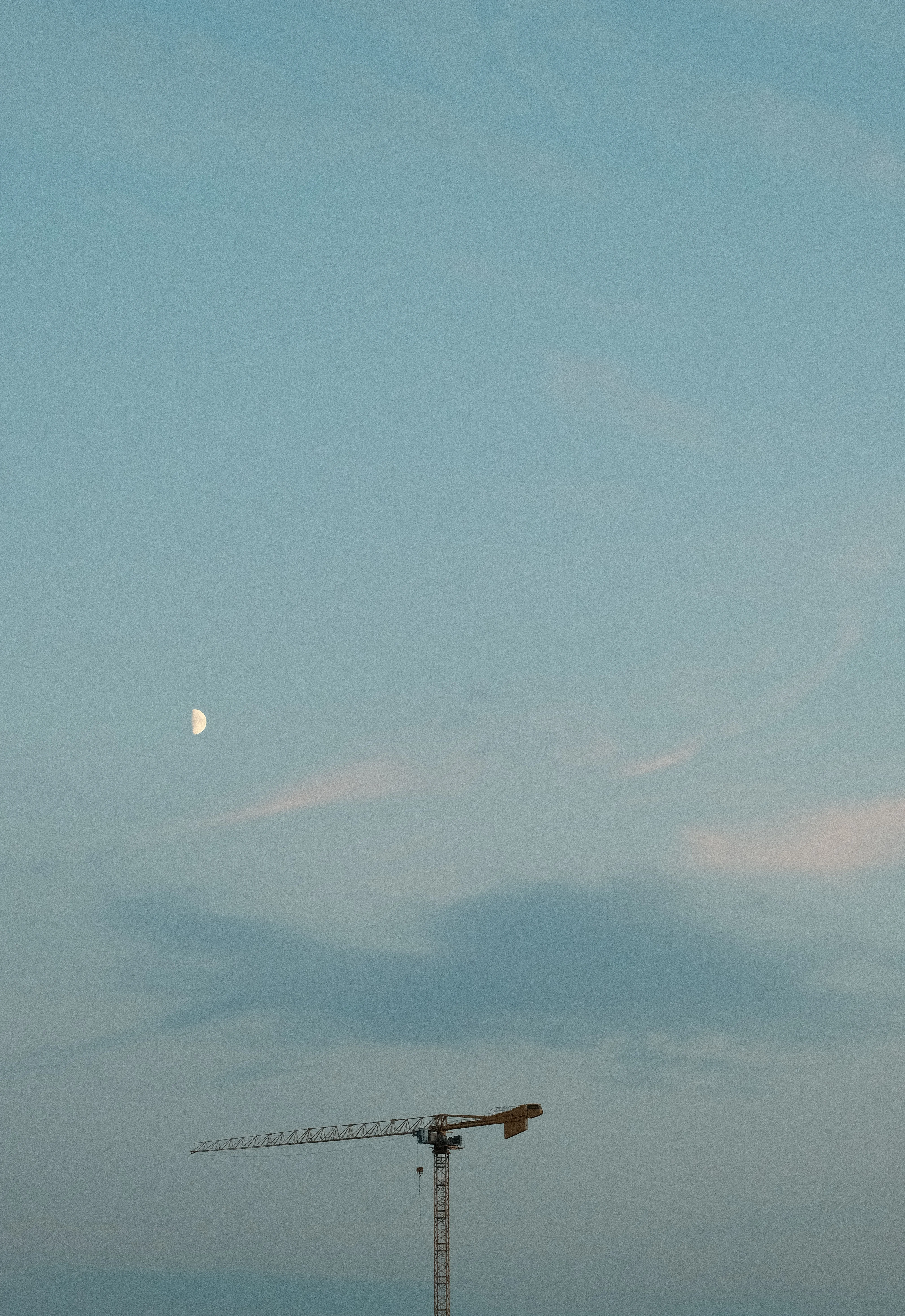 A photo of a construction crane silhouetted against a twilight sky with a crescent moon and light clouds