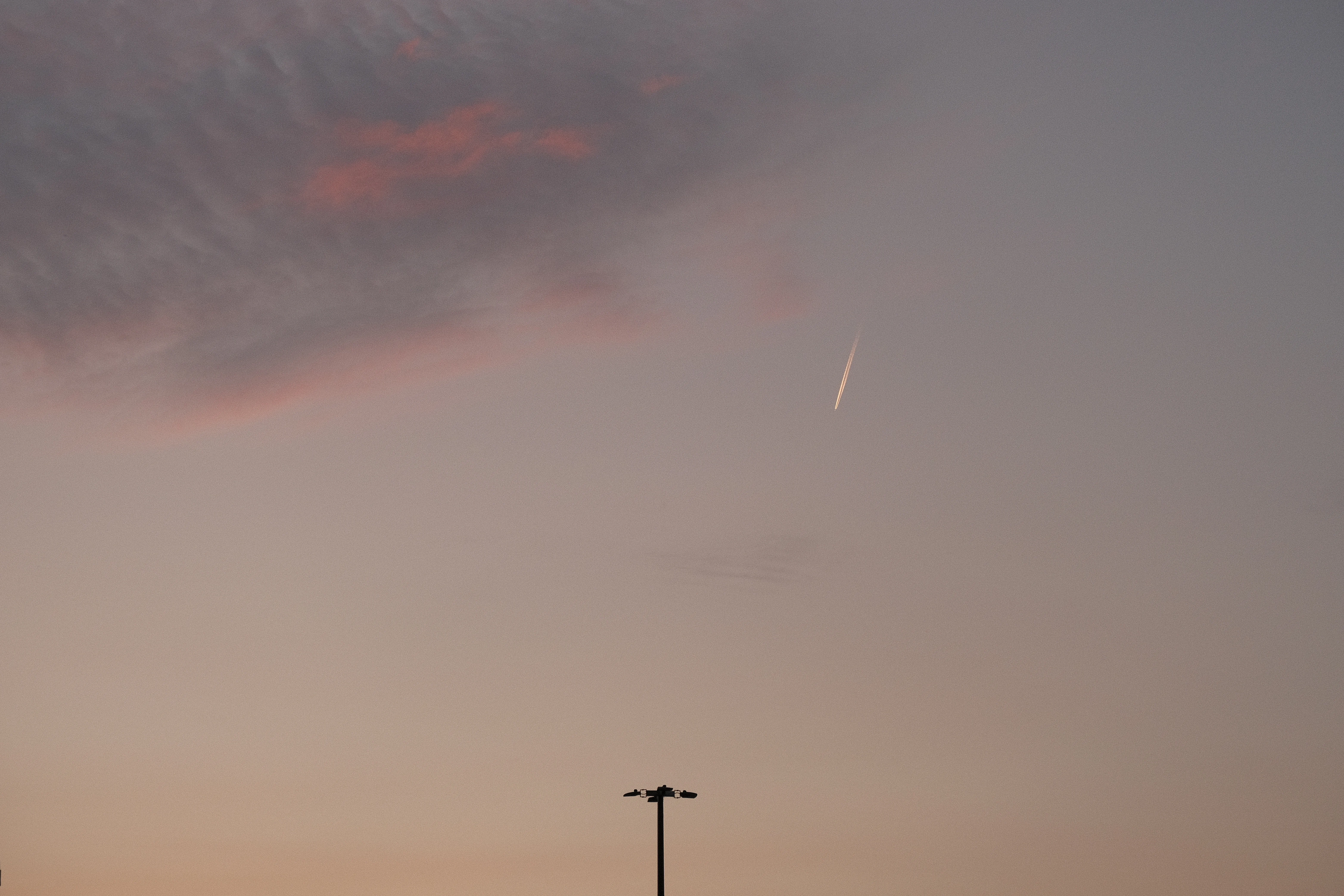 A photo of a shooting star streaking across a dusky sky, with a light pole silhouetted in the foreground.