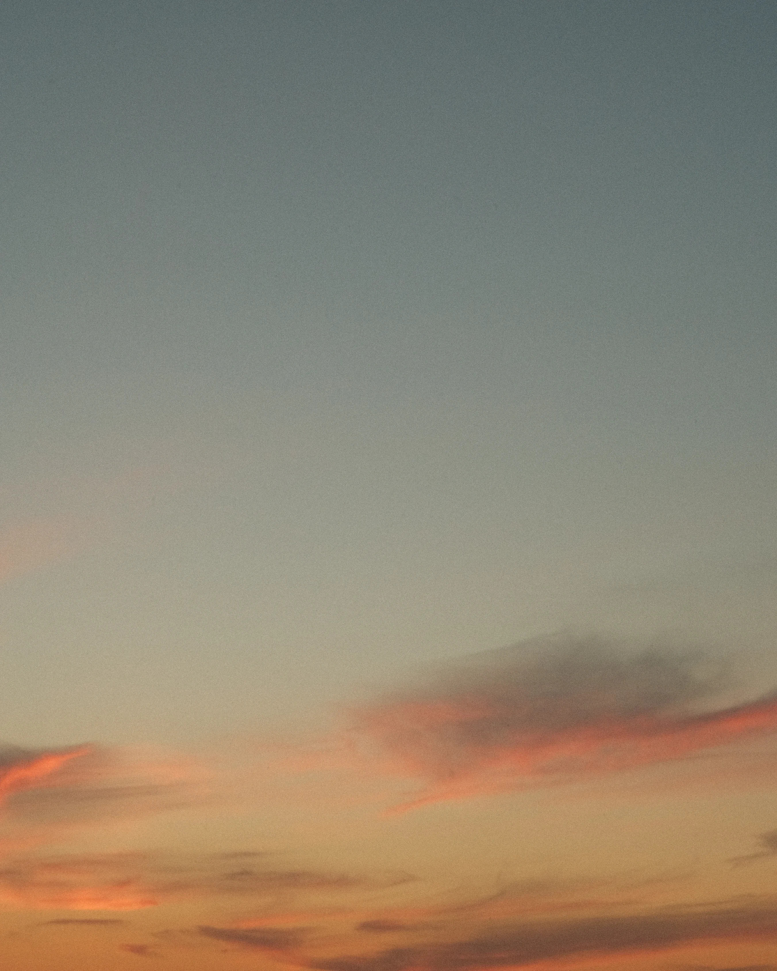 A photo of a sunset sky with orange and pink hues near the horizon. The sky is mostly clear with faint, wispy clouds.